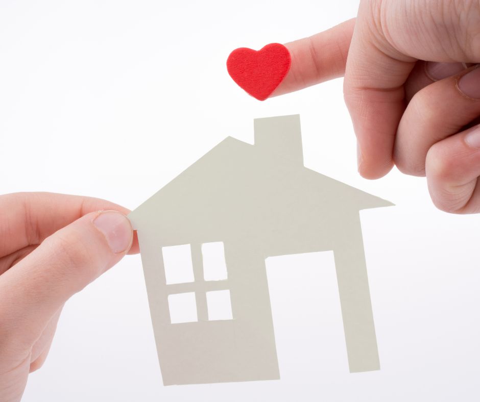 House made of paper with someone adding a red heart to the chimney.