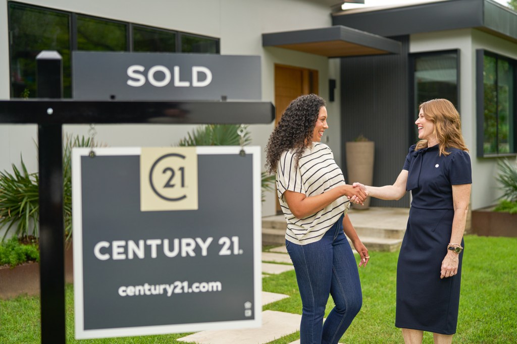 Agent shaking hands with a client next to a Century 21 For Sale sign.